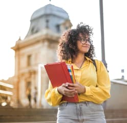 Female student holding books in front of a school building
