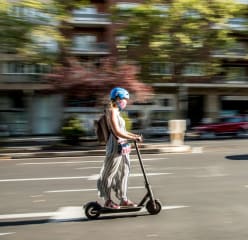 A woman driving a scooter in the middle of a boston road.