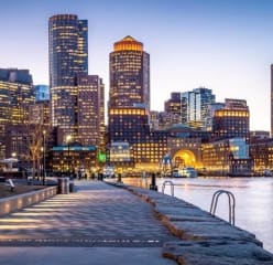 boston city skyline at night with all the buildings lit up and a body of water in the right half of the image