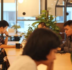 People working in a coworking space with rooms separated by glass walls.