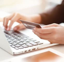woman holding credit card implying online payment with white laptop