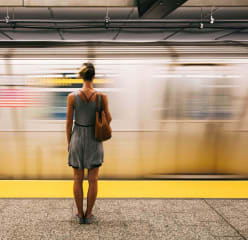 Woman in a grey dress with bare legs standing with her back to the camera, facing a fast moving train