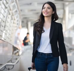 business travel - young woman with hand luggage walking down sidewalk in urban city
