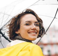 woman smiling, holding an umbrella and wearing a yellow rainjacket