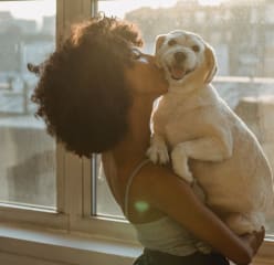 woman hugging her dog and kissing his cheek while he looks at the camera smiling