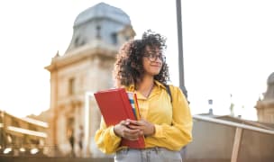 Female student holding books in front of a school building