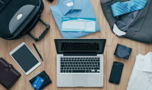 shot from above, showing a table with a laptop, a phone, a small suitcase, some shirts, ties and a couple of wallets