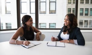two women sit at a table and take notes