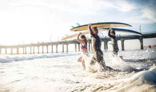 three people holding surfboards above their heads walk out into the water near the pier in Los Angeles