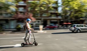 A woman driving a scooter in the middle of a boston road.