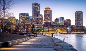 boston city skyline at night with all the buildings lit up and a body of water in the right half of the image