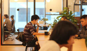 People working in a coworking space with rooms separated by glass walls.