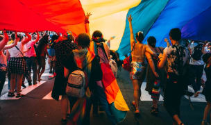 people marching down a road with a giant pride flag overhead