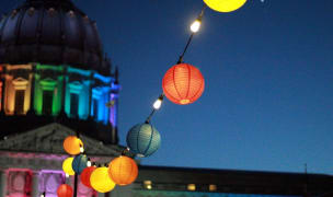 The san francisco city hall at night lit in the rainbow colors of the pride flag.