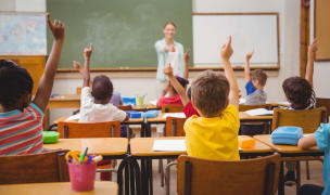 young pupils raising their hands during class teacher pointing at child in yellow