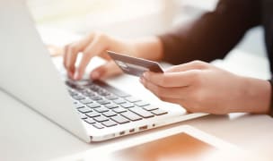 woman holding credit card implying online payment with white laptop