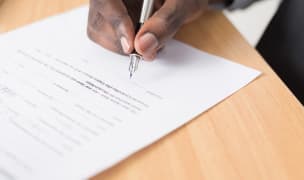 The hand of a man signing a contract with a pen.