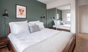 small bedroom with a double bed, a large mirror next to the bed, green accent wall and two nightstands with lamps