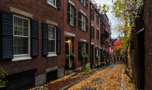 alley with brownstones with autumn brown leaves on the ground, moody weather, and a US flag hanging from a house down the alley