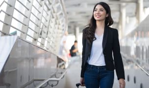 business travel - young woman with hand luggage walking down sidewalk in urban city
