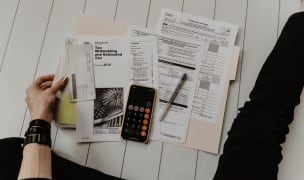 A person sitting on a white wood floor working on various tax forms.