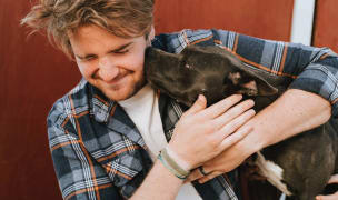 man hugging a Pitbull puppy and it's licking his face