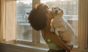 woman hugging her dog and kissing his cheek while he looks at the camera smiling