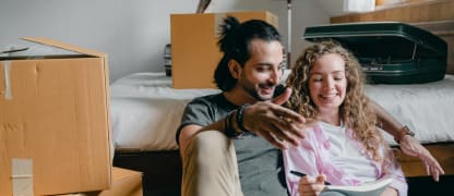 A couple sitting near a bed and moving boxes