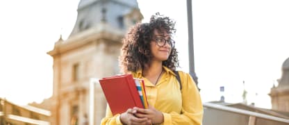 Female student holding books in front of a school building