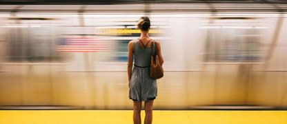 Woman in a grey dress with bare legs standing with her back to the camera, facing a fast moving train