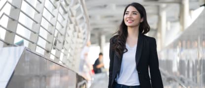 business travel - young woman with hand luggage walking down sidewalk in urban city