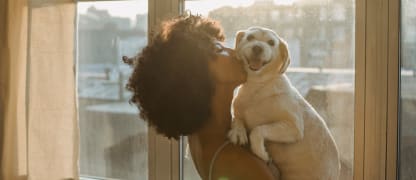woman hugging her dog and kissing his cheek while he looks at the camera smiling
