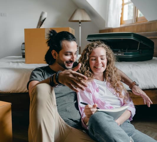 A couple sitting near a bed and moving boxes