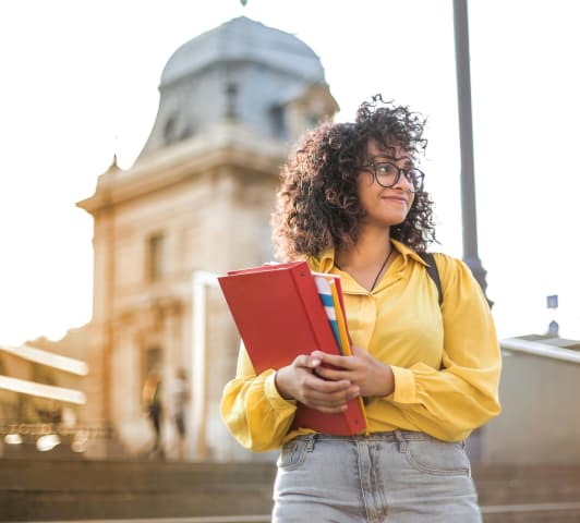 Female student holding books in front of a school building