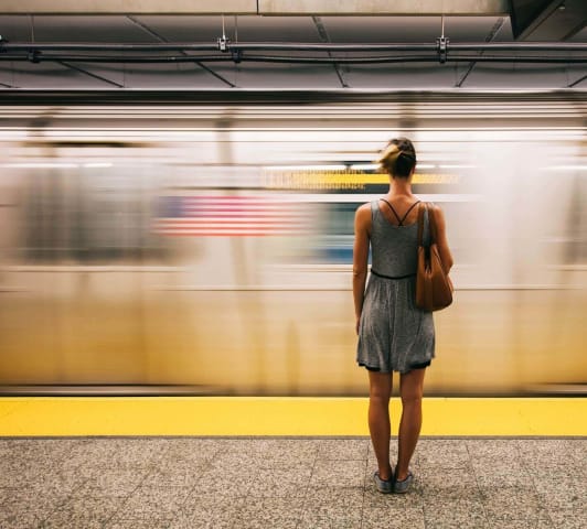 Woman in a grey dress with bare legs standing with her back to the camera, facing a fast moving train