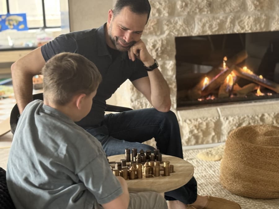 Dad and son playing chess by the fireplace