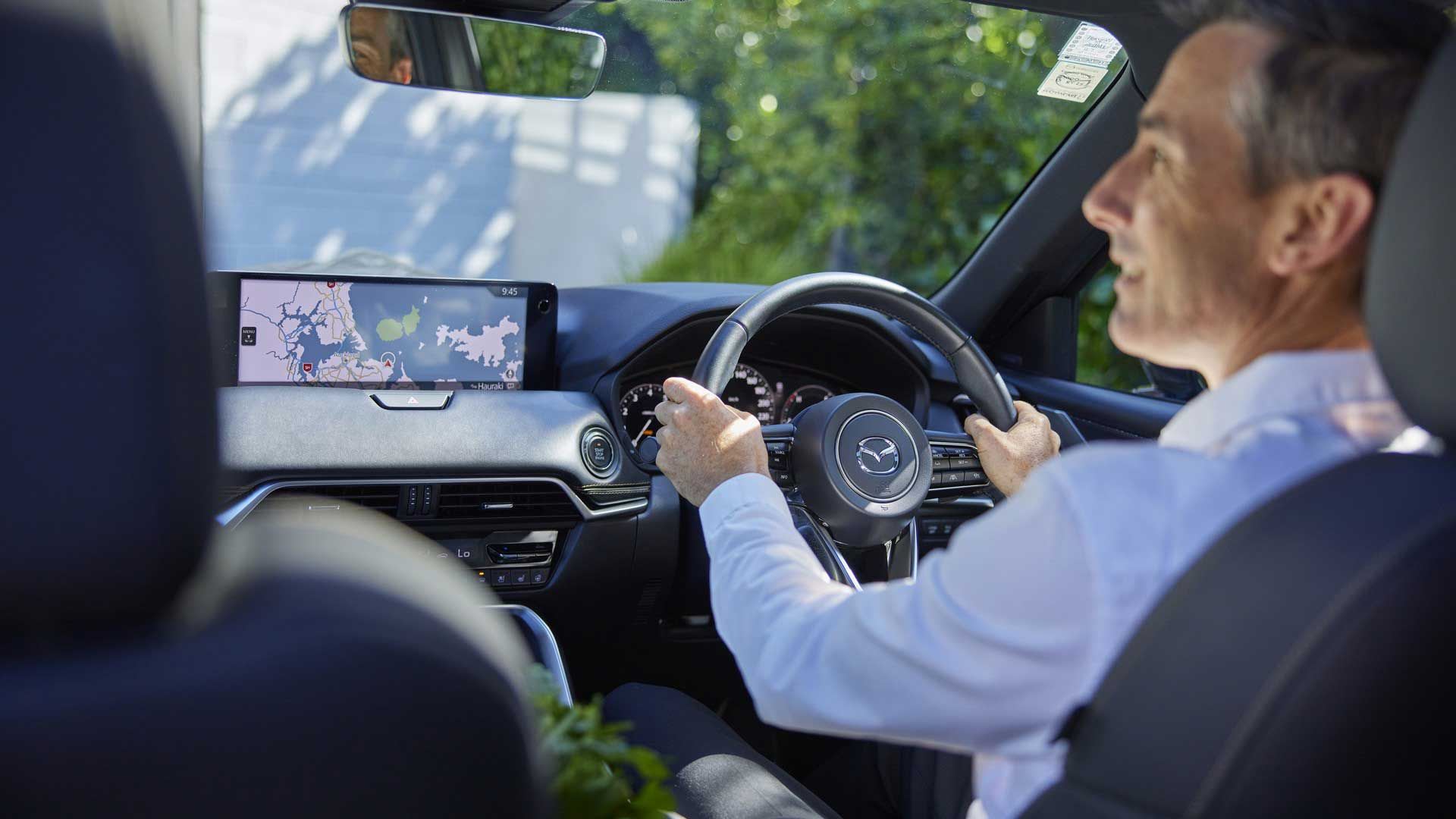 Man driving a Mazda CX-90 SUV as seen from the rear seat