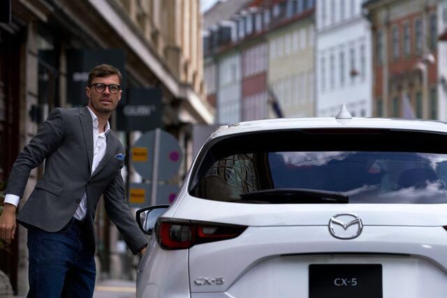 Close up of the rear of a white Mazda CX-5 SUV with a man in a suit standing next to the car