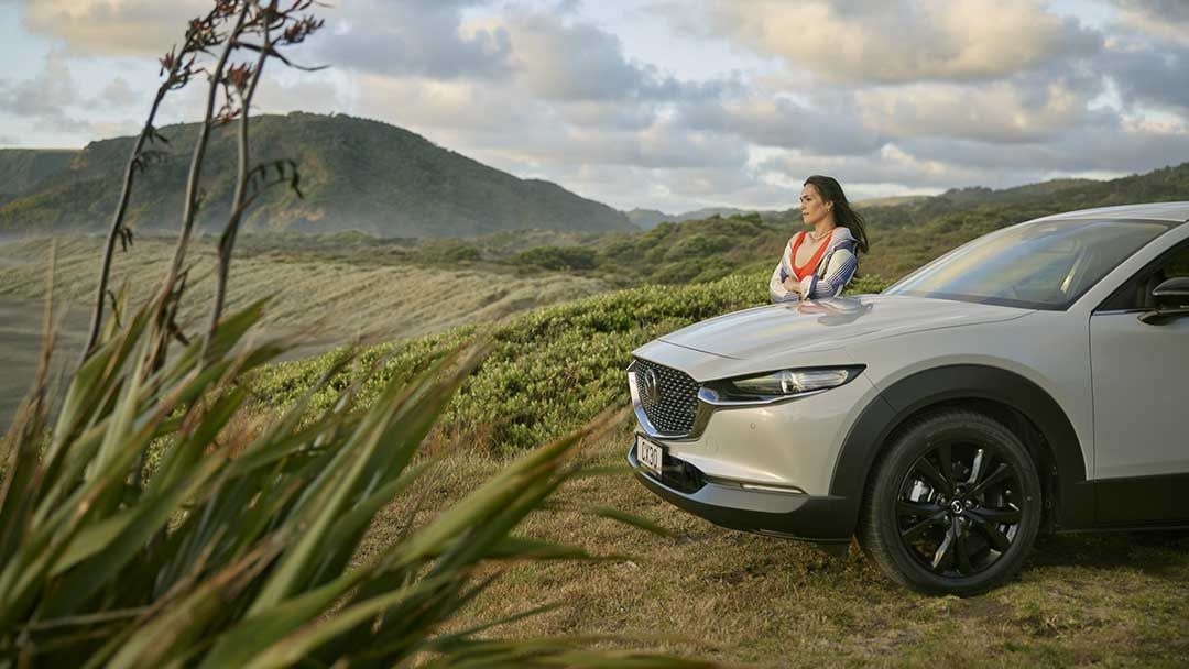 Woman standing next to her white Mazda CX-30 SUV parked at a mountain lookout