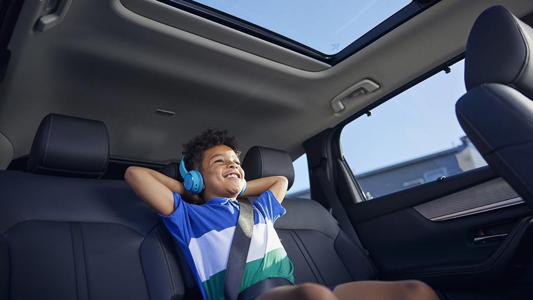 Looking back at a boy in the middle rear seat of his family's Mazda CX-80 SUV
