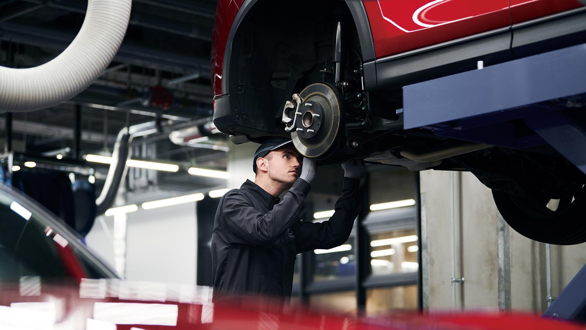 Mazda service technician working on a Mazda vehicle that is raised on a hoist in a Mazda service centre