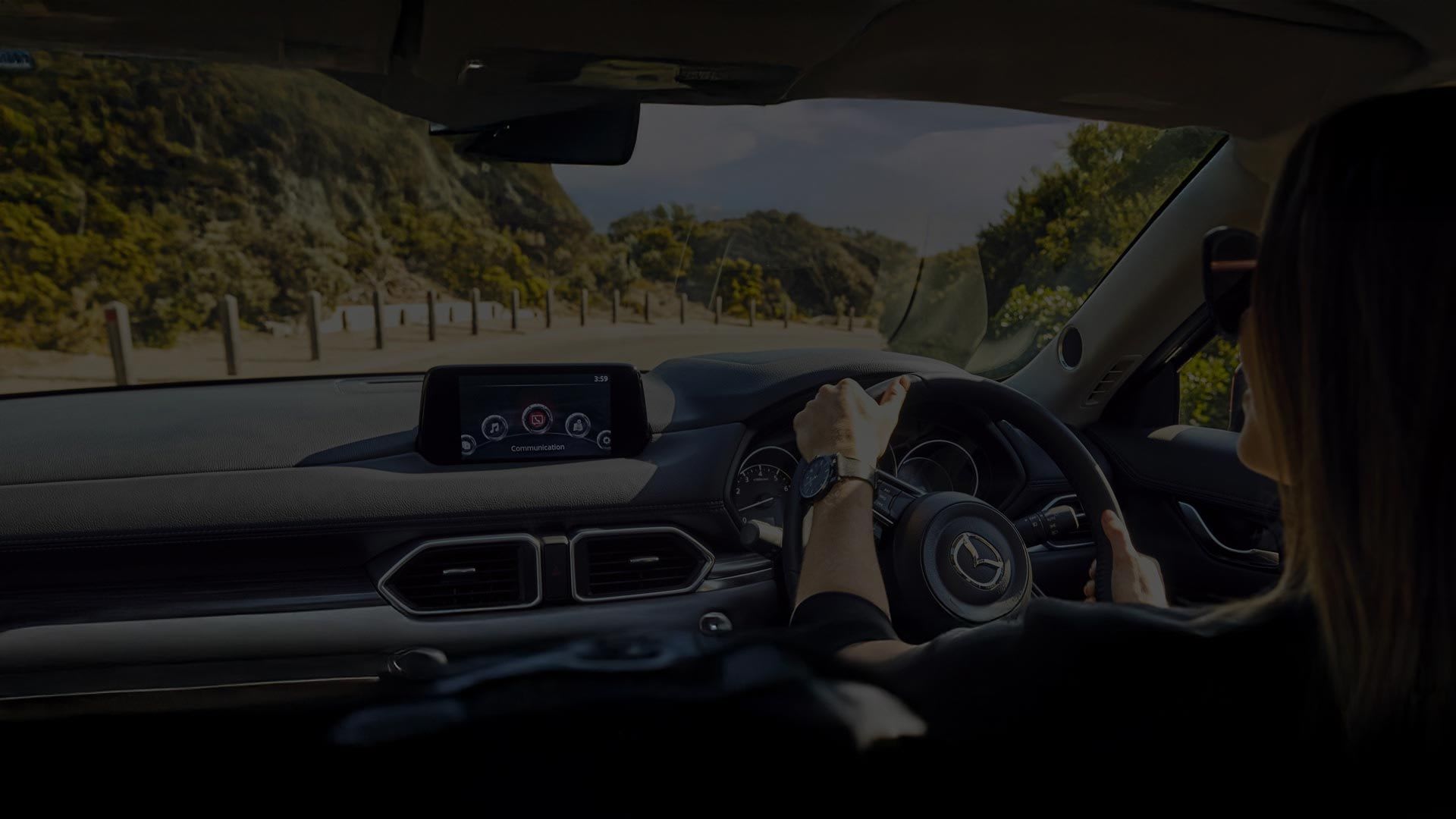 Looking from the rear seat of a woman driving her Mazda and the view of the country road through the windscreen
