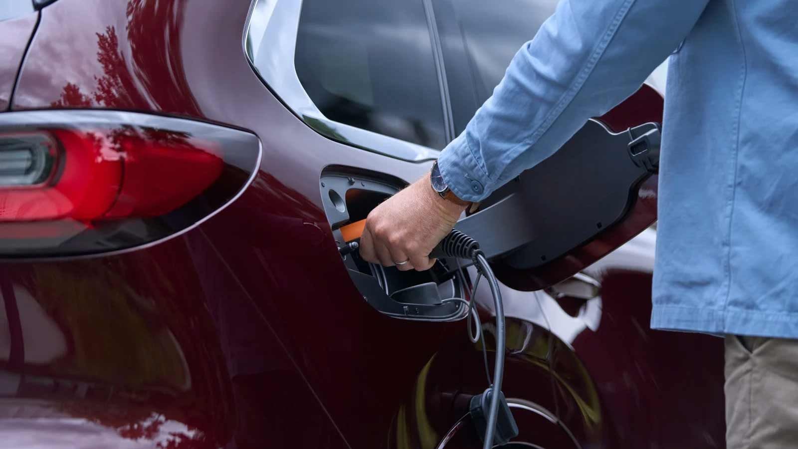 Close-up of a man charging his Artisan Red Mazda CX-80 7-seat plug-in hybrid SUV 