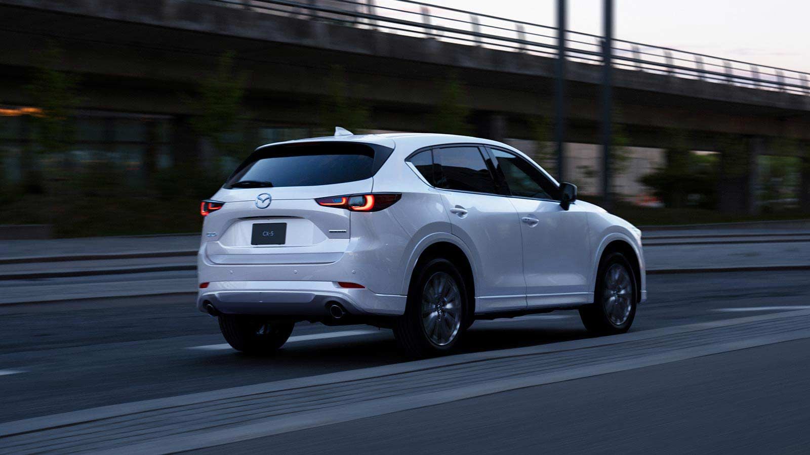 Rear three-quarter view of an Arctic White Mazda CX-5 SUV driving on the freeway