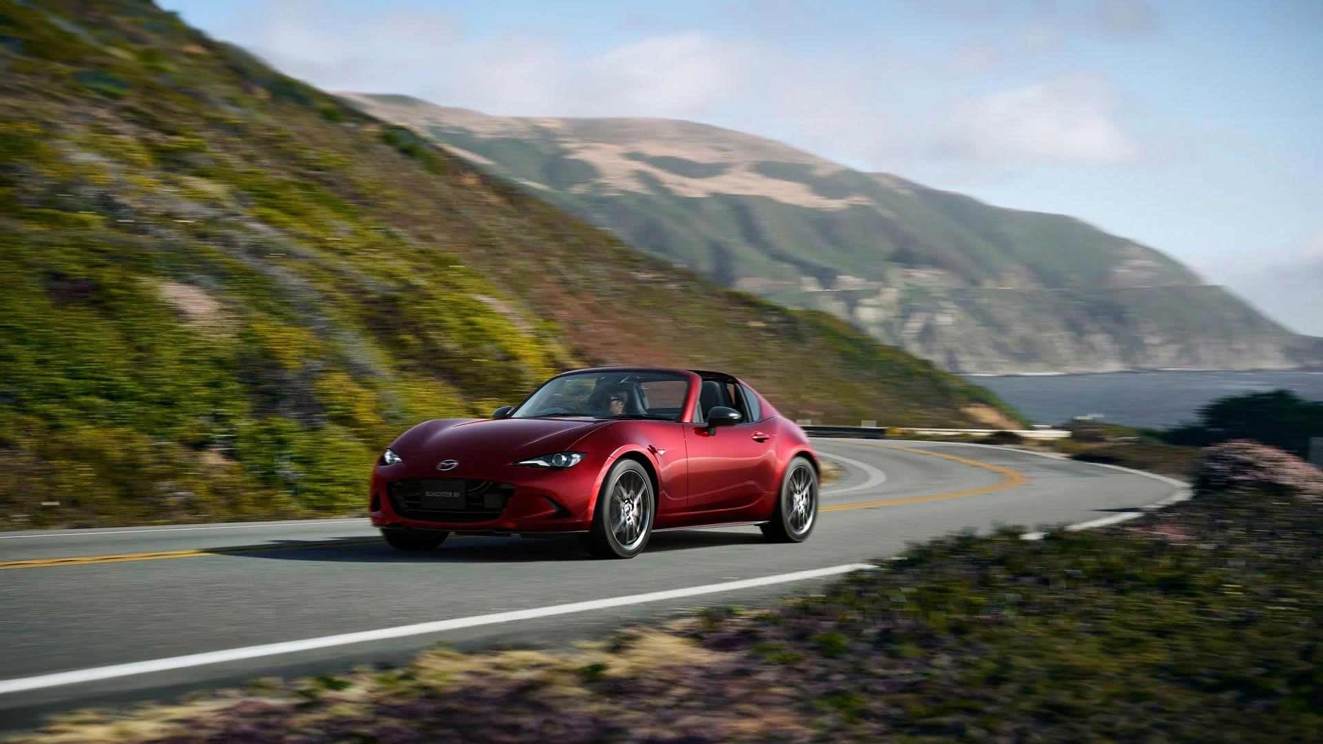 Front three-quarter view of a Soul Red Mazda MX-5 RF sports car driving on a winding mountain road