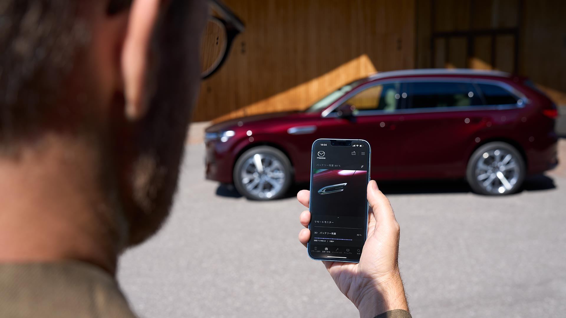 Man holding his smartphone with his Artisan Red Mazda CX-80 SUV parked in the background