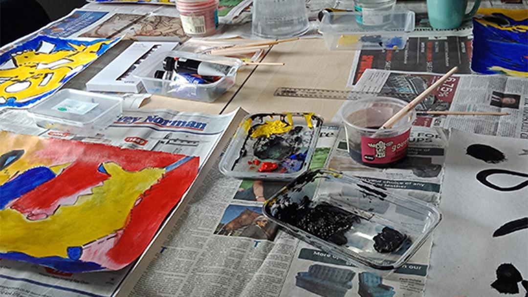 Paint palette, paint brushes and paint tins sitting on a table covered in newspaper - Mazda Foundation 2020 grant recipients  