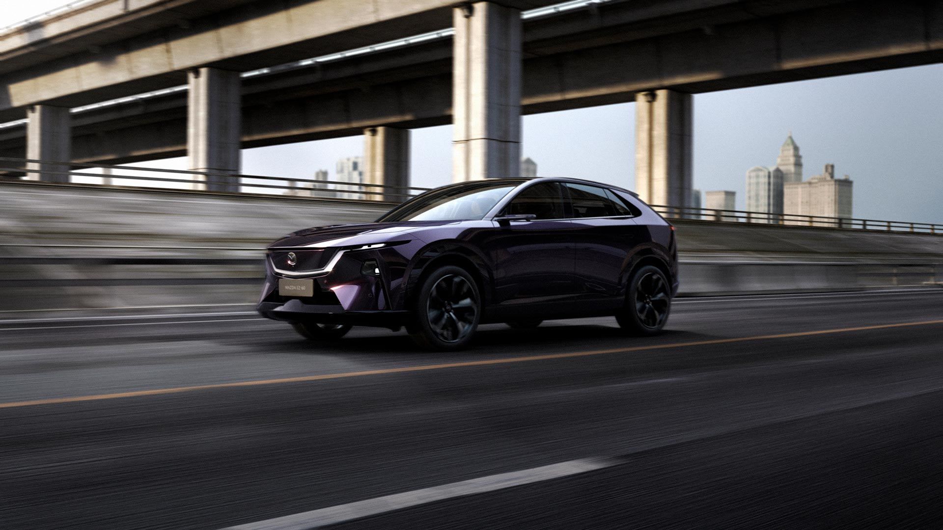 Front three-quarter view of a purple Mazda EZ-60 electric SUV driving on a freeway under an overpass