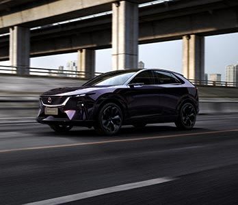 Front three quarter view of a purple Mazda EZ-60 Electric SUV driving on a freeway underpass