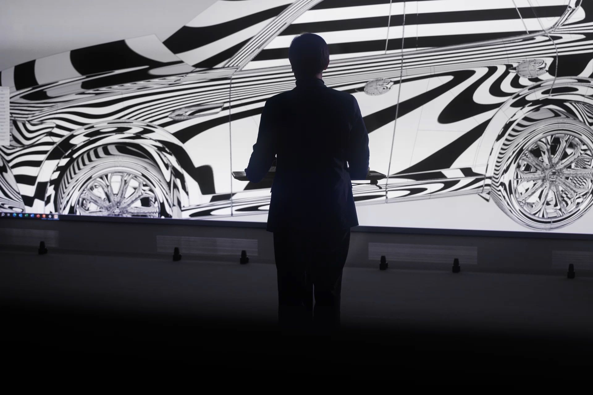 Silhouette of a man standing in front of a large screen showing a Mazda design